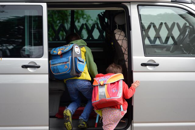 Kinder mit Schultornistern klettern in ein Auto.