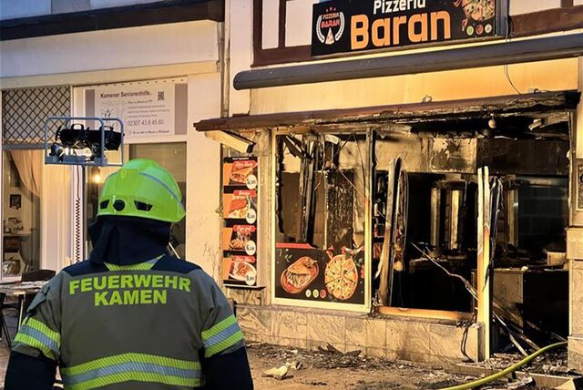 Ein Feuerwehrmann steht mit dem Rücken zur Kamera, den Blick auf die ausgebrannte Pizzeria Baran in der Kamener Innenstadt gerichtet.