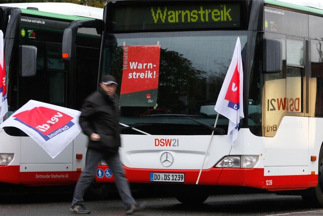 Ein streikender Busfahrer läuft mit einer Flagge der Gewerkschaft Verdi an einem Bus vorbei.