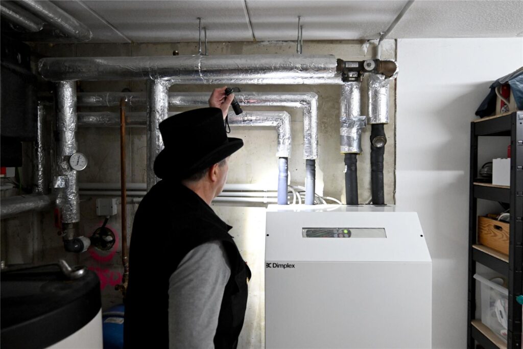 Ein Schornsteinfeger überprüft eine Wärmepumpe. Ein Schornsteinfeger überprüft eine Wärmepumpe.