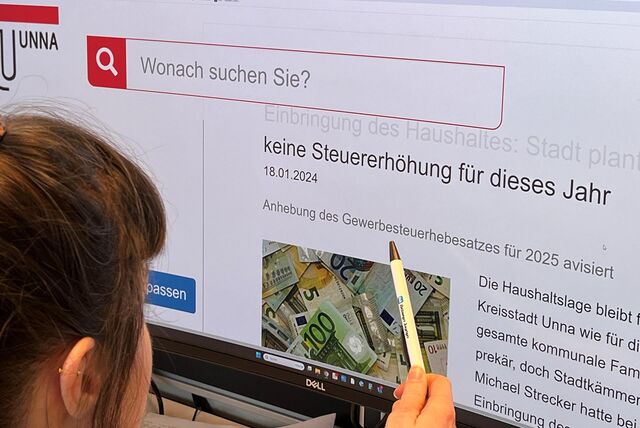 Eine junge Frau sitzt mit einem Kugelschreiber des Hellweger Anzeigers in der rechten Hand vor einem Computerbildschirm, auf dem die Internetseite der KReisstadt Unna zu sehen ist.