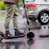 Ein Mann fährt mit einem E-Scooter neben einem Auto auf der Straße.