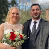 Am Hertener Standesamt stehen Sarah König und Murat Aslan nebeneinander und lächeln freundlich in die Kamera. Sie hält einen Brautstrauß in ihrer rechten Hand.
