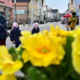 Menschen gehen auf der Massener Straße durch die Fußgängerzone in Unna. Im Vordergrund sind gelbe Blumen.