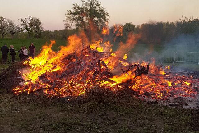 Ein großes Osterfeuer lodert in Wasserkurl. Im Hintergrund stehen Menschen.