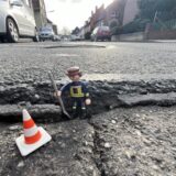 Ein Playmobil-Männchen steht in einem Schlagloch auf einer Straße.