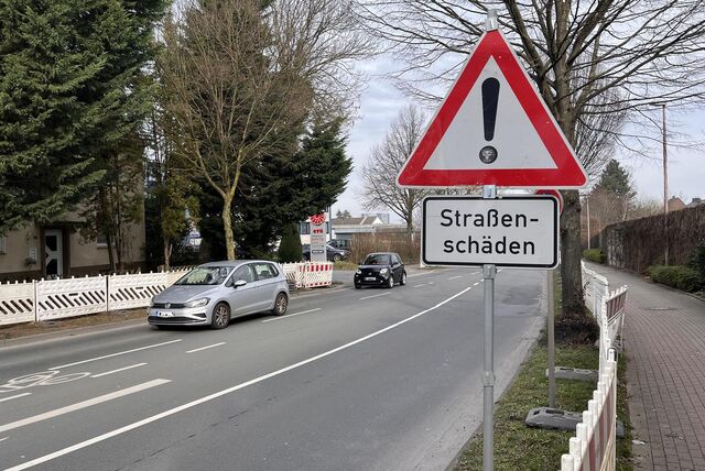 An der Straße Büddenberg in Unna weist ein Warnschild auf Straßenschäden hin. Zwei Autos fahren über die Straße. Auf beiden Seiten stehen Absperrungen.