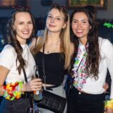 Drei gut gelaunte, junge Frauen mit Sonnenbrillen, Blumenketten und Alkoholischen getränken.