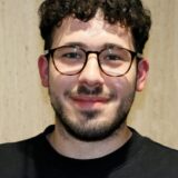 Ein Porträt von Cem Baykan (21), Beisitzer im VfL-Vorstand. Ein junger Mann mit kurzen, lockigen und braunen haaren, runter brauner Brille und kurzem Vollbart.