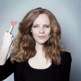 Kabarettistin Sarah Bosetti zeigt mit ihrer rechten Hand den Mittelfinger, der mit einem Herz überdeckt ist.