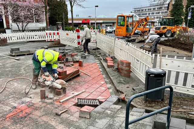 Bauarbeiter arbeiten am Königsborner Tor in Unna an der Pflasterung. Im Hintergrund stehen ein Bagger und ein Radlader
