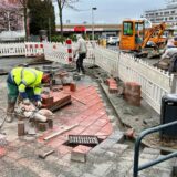 Bauarbeiter arbeiten am Königsborner Tor in Unna an der Pflasterung. Im Hintergrund stehen ein Bagger und ein Radlader