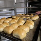 Eine Ladung frisch gebackene Brötchen liegt auf einem Ofenblech in einer Bäckerei.