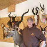 Der Tierpräparator Michael Hesse-Siebigteroth steht im Showroom seines Unternehmens in Waltrop vor einer Wand, an der verschiedene ausgestopfte Tiere hängen. Neben heimischen Tieren wie Dachs und Fuchs auch Antilopen.