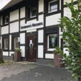 Collage: Links ist das leerstehende Landhaus Hellweg in Unna abgebildet, rechts zeigt der Dortmunder Koch Kay Fräder auf ein Plakat.