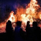 Schattenspiel von Menschen vor dem Osterfeuer in Overberge, das Funken in die Nacht entsendet.