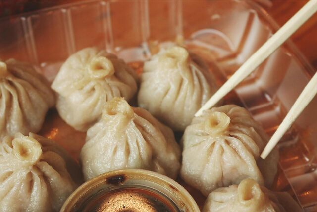 Teigtaschen, auch Dumplings genannt, liegen in einer Schale und werden mit Stäbchen gegessen.