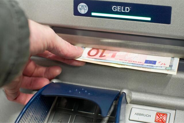 Eine Hand greift nach Geldscheinen, die gerade aus einem Bankautomaten kommen.