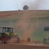 Ein Bauer wirbelt beim Eggen Staub von einem trockenen Acker auf.