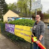Eine Frau steht vor dem Schulhof der Pfalzschule in Bergkamen-Weddinghofen. Am Zaun hängt ein Transparent mit der Aufschrift „Zu Fuß zur Schule. Frische Luft statt Elterntaxi“