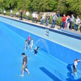 Besucher laufen im Freibad Dellwig durch das große Becken, während das Wasser hineinfließt