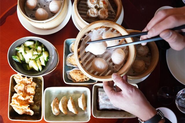 Ein Mann greift in einem chinesischen Restaurant mit Essstäbchen nach Dim sum, gedämpfte Teigtaschen, die in einem Bambuskorb liegen.