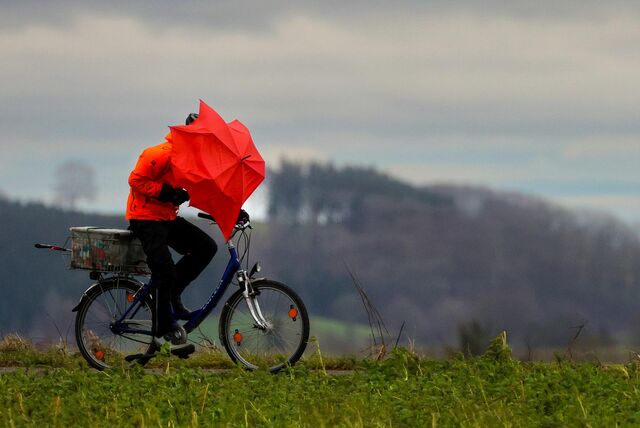 Ein Radfahrer ist bei Regen und Sturm mit einem Regenschirm unterwegs.
