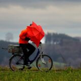 Ein Radfahrer ist bei Regen und Sturm mit einem Regenschirm unterwegs.