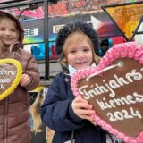 Frühjahrskirmes 2024 in Unna: Zwei Kinder halten Lebkuchenherzen. Im Hintergrund ist ein Kirmes-Fahrgeschäft.