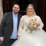 Das Brautpaar Natalie Langer und Kevin Langner-Steuer steht nach der Zeremonie vor der St. Antonius-Kirche in Herten und lächelt freundliche in die Kamera.