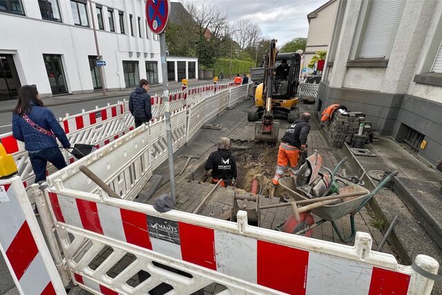 Bauarbeiter arbeiten in einer Baugrube im Bürgersteig des Ostrings in Unna. Fußgänger nutzen einen provisorischen Weg zwischen rot-weißen Baken.