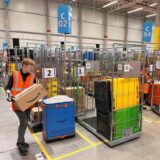 Eine Amazon-Mitarbeiterin trägt im Verteilzentrum Unna ein Paket in einen Transportwagen.