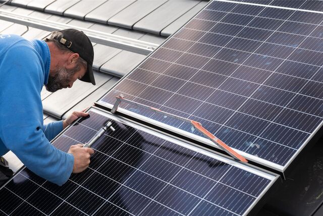 Ein Handwerker bringt eine Photovoltaikanlage auf einem Dach an.