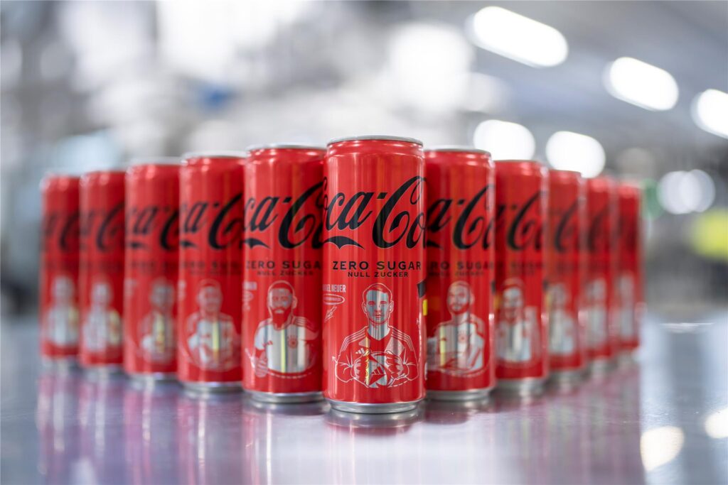 Coca-Cola-Dosen stehen aufgereiht auf einem Tisch. Das Gesicht von Fußball-Nationaltorhüter Manuel Neuer ist auf der ersten Dose zu sehen. Coca-Cola-Dosen stehen aufgereiht auf einem Tisch. Das Gesicht von Fußball-Nationaltorhüter Manuel Neuer ist auf der ersten Dose zu sehen.