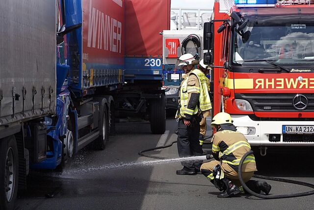 Nach einem Unfall am Montag (29.04.) sind Feuerwehrleute auf der Autobahn 1 zwischen Kamen und Unna im Einsatz. Ein Feuerwehrmann spritzt Wasser unter die demolierte Zugmaschine eines Lastwagens.