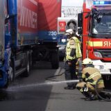Nach einem Unfall am Montag (29.04.) sind Feuerwehrleute auf der Autobahn 1 zwischen Kamen und Unna im Einsatz. Ein Feuerwehrmann spritzt Wasser unter die demolierte Zugmaschine eines Lastwagens.