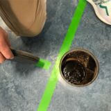 Ein Mann hockt in den Hellwegsporthallen in Unna neben einer runden Öffnung im Boden. Darin steht Wasser.