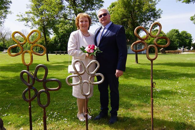 Das Brautpaar steht auf einer Wiese, während metallene Blumen des Kettenschmiedemuseums im Vordergrund zu sehen sind.