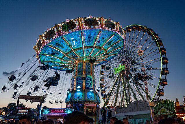 Auf der Cranger Kirmes in Herne drehen sich ein Kettenkarussell und Riesenrad im Abendlicht der blauen Stunde.