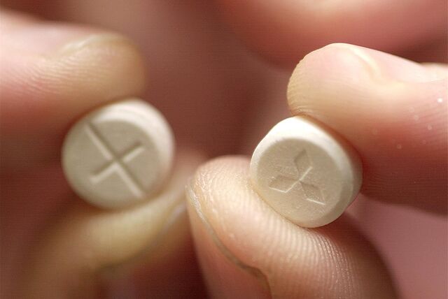 Jemand hält zwei Ecstasy-Tabletten für eine Nahaufnahme in die Kamera.