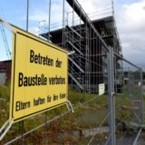 An einem Bauzaun hängt ein gelbes Schild mit schwarzer Schrift: „Betreten der Baustelle verboten. Eltern haften für ihre Kinder.“