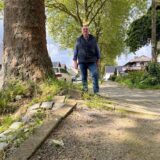 Gilbert Vogt steht in Unna an der Dorotheenstraße auf einem teils zerstörten Gehweg. Der Baum links hat Steine und Platten angehoben.