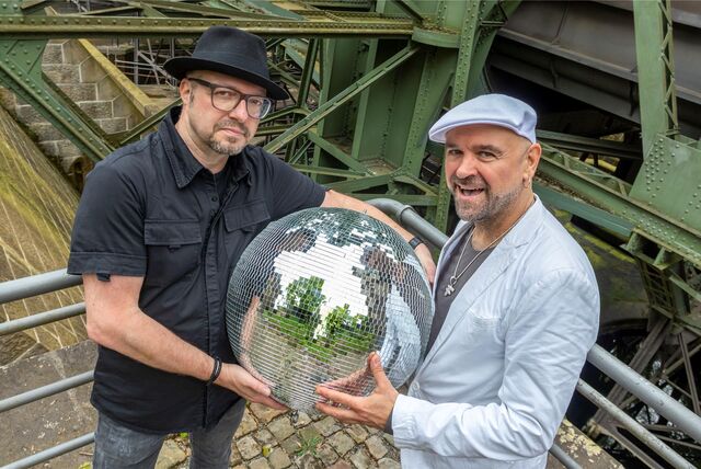 Zwei Männer stehen auf dem Gelände des Alten Schiffshebewerks in Henrichenburg und halten eine Discokugel in den Händen.