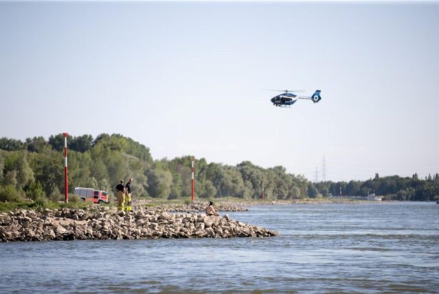 Aus einem Hubschrauber und vom Ufer aus suchen Einsatzkräfte nach einem Schwimmer, der im Rhein von einem Sog erfasst und mitgerissen wurde.