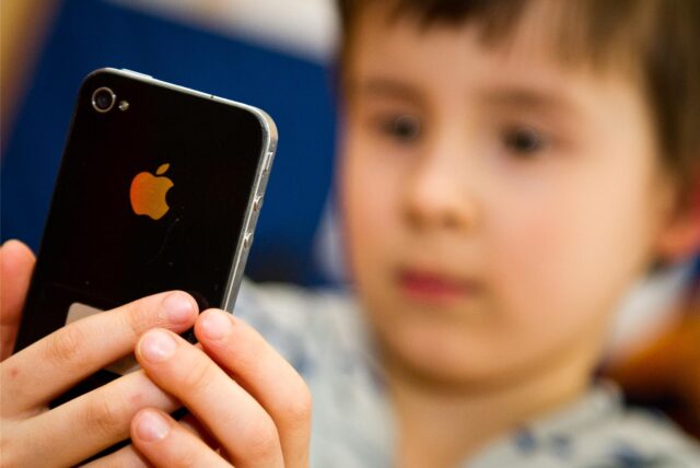 Ein Junge blickt auf den Bildschirm eines iPhones, das er in seinen Händen hält.
