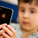 Ein Junge blickt auf den Bildschirm eines iPhones, das er in seinen Händen hält.