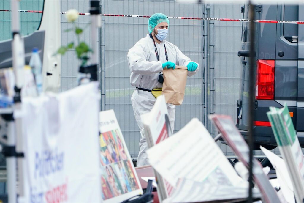Ein Mitarbeiter der Spurensicherung hält hinter umgeworfenen Plakaten eines Standes eine Tüte in den Händen. Ein Mitarbeiter der Spurensicherung hält hinter umgeworfenen Plakaten eines Standes eine Tüte in den Händen.
