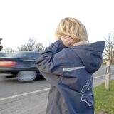Ein Kind hält sich die Ohren zu, als Autos auf einer Straße an ihm vorbeifahren.