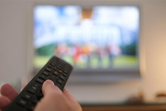 Eine Person mit einer Fernbedienung vor dem Fernseher (Symbolbild).