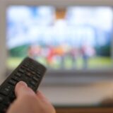 Eine Person mit einer Fernbedienung vor dem Fernseher (Symbolbild).